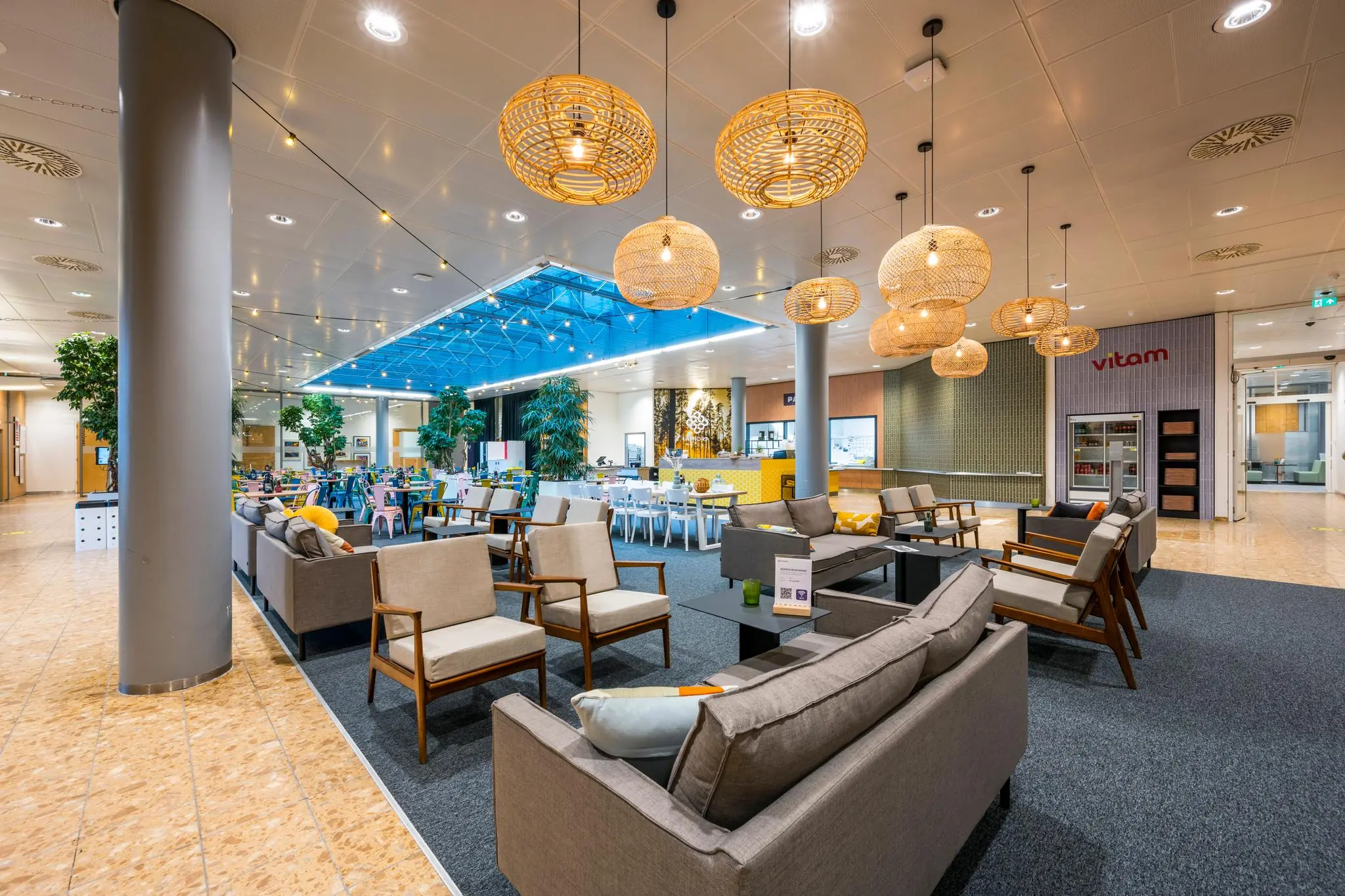 Moderne en sfeervol ingerichte zit- en eetruimte aan de Burgemeester Rijnderslaan met loungehoeken, hanglampen en het restaurant Vitam op de achtergrond.